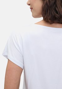 Chemise blanche à manches courtes avec un large col et une texture douce et lisse, montrant l'arrière du vêtement et la zone des épaules.