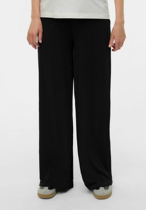 Weite schwarze Hosen aus weichem Material, mit lockerer Passform und gerader Silhouette. Kombiniert mit grauen Sneakern für einen lässigen Look.