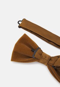 Brun fløyelsbowtie med teksturert finish og en svart lås. Akkompagnert av et matchende stoffstropp.