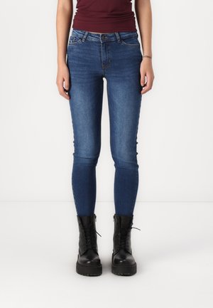 Blue denim skinny jeans with a mid-rise waist, five-pocket design, and subtle stitching details, paired with black lace-up boots.