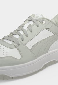 Κοντινό πλάνο ενός λευκού και ανοιχτόγκρι sneaker Puma με κορδόνια, πάνελς από σουέντ και δέρμα και μια υφασμένη λαστιχένια σόλα.