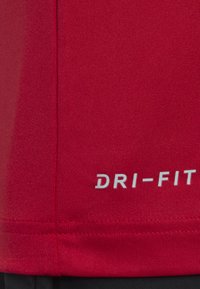 Camiseta atlética roja Dri-FIT con tejido texturizado, costuras suaves y un logo Dri-FIT visible en blanco en la parte inferior derecha.