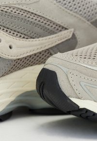 Bežinės sportinės bateliai, pagaminti iš tinklinės ir zoliukės medžiagų, su tekstūruotomis paviršiais, guminiais padais ir sudėtingais siuvinėjimo akcentais.