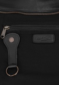 Black fabric bag section with metal zipper, leather key holder strap with ring, and stitched label reading "Gusti Leder studio."