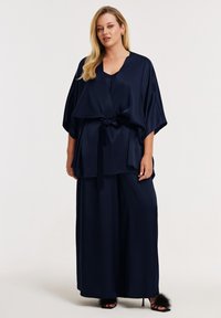 Haut kimono en satin bleu marine avec manches larges, taille ceinturée, et pantalon large assorti. Texture douce avec une finition lisse.