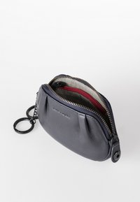 Portamonete in pelle di colore blu navy, dotato di chiusura con zip, interno a righe e attacco per portachiavi. Superficie liscia con dettagli sottili.