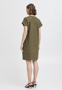 Vestido de lino verde oliva con mangas cortas y un corte relajado, con un detalle de costura en la parte superior de la espalda y un dobladillo recto.