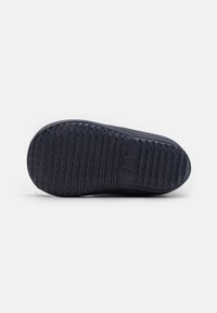 Suela de goma negra con patrón de espiga texturizado. Tacón ligeramente elevado, bordes suaves y estampado del logo en el centro.