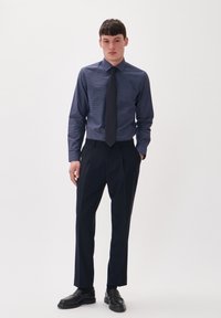 Tengerész mintás ing hosszú ujjal, gallérral és vékony nyakkendővel, sötét, elegáns nadrággal és fekete mokaszin cipővel párosítva.
