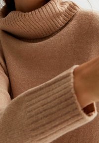 Pull à col roulé beige en tissu tricoté doux. Caractéristiques : col et poignets côtelés, texture lisse et coupe décontractée.