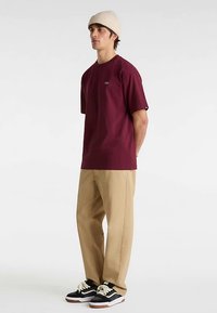 Bordowa koszulka z krótkim rękawem i dekoltem typu crew, zestawiona z khaki spodniami oraz czarno-białymi trampkami, do tego beżowa dzianinowa czapka.