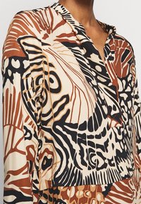 Camicia a maniche lunghe caratterizzata da un collage di motivi astratti in marrone, nero e crema; tessuto testurizzato con colletto e bottoni.