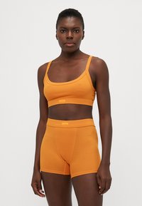 Set di reggiseno sportivo a coste arancioni e pantaloni corti a vita alta. Il tessuto è morbido con una consistenza delicata e una vestibilità aderente, caratterizzato da spalline sottili e senza accessori prominenti.