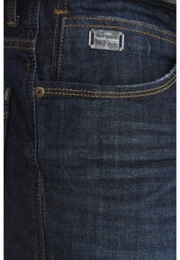 Temne modre denim hlače z oranžnim šivom, srebrno kovinsko oznako z graviranim blagovno znamko in dizajnom s petimi žepi.