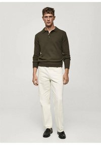 Dark green knitted polo sweater with a slim fit, paired with white tailored pants and black leather shoes, standing against a light background.