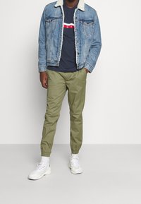 Jeansjacka med fårskinnskrage, marinblå t-shirt med röd och vit detalljering, olivgröna joggers och vita sneakers.