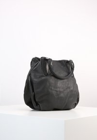 Czarna skórzana torebka z krótkimi uchwytami, miękką fakturą i lekko opadającym kształtem, umieszczona na białym piedestale na jednolitym tle.