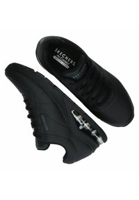 Sneakers Skechers neri con tomaia sintetica liscia, dettagli perforati, chiusura con lacci e ammortizzazione visibile nella suola.