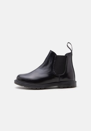 Bottes Chelsea en cuir noir avec panneaux latéraux élastiques, languette au talon et semelle en caoutchouc basse sur fond uni.