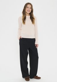 Light pink knit sweater with textured stitch detailing, paired with loose black trousers and brown moccasin-style slippers.