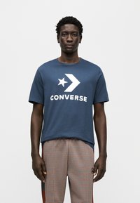 Μπλε σκούρο βαμβακερό t-shirt με μεγάλο λευκό λογότυπο "CONVERSE" και σχέδιο αστεριού στο μπροστινό μέρος, συνδυασμένο με παντελόνι με μοτίβα.