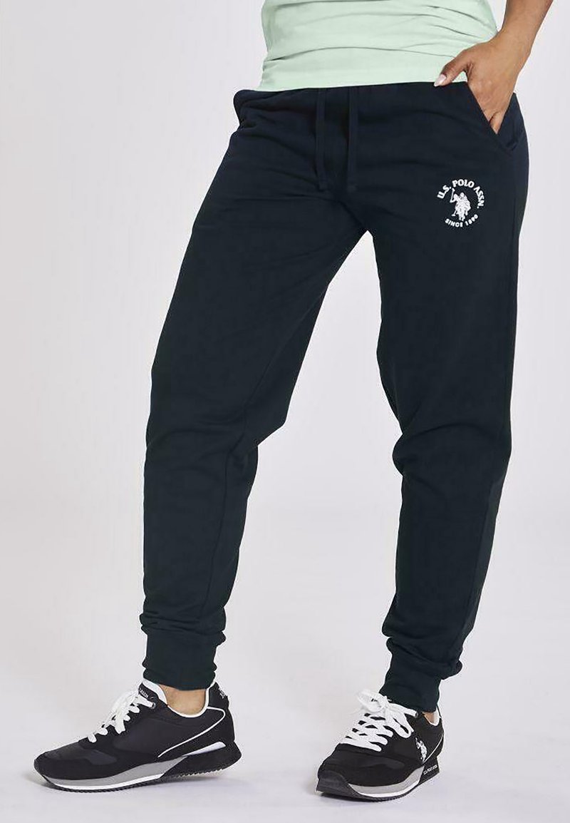 Pantalones de chándal azul marino oscuro hechos de un tejido suave y elástico, con una cinturilla elástica, bolsillos laterales y un logo blanco en el muslo.