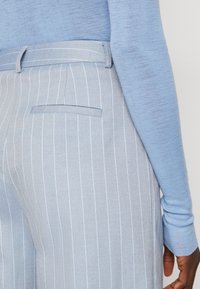 Lichtblauw brei-top gecombineerd met lichtblauwe gestreepte broek. De broek heeft een achterzak en een getailleerde tailleband. Geweven stof is zichtbaar.