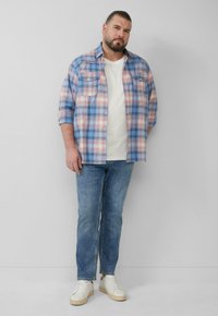 Hellblaues und pinkes kariertes Flanellhemd mit zwei Brusttaschen, getragen über einem weißen Rundhalsausschnitt-T-Shirt, kombiniert mit hellblauen Jeans und weißen Turnschuhen.