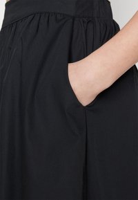 Falda negra con cintura fruncida y bolsillo lateral. Textura suave con un acabado liso, que enfatiza una forma simple y clásica.