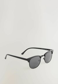 Ochelari de soare rotunzi cu o ramă din plastic negru, lentile întunecate și tampoane nazale transparente. Brațe subțiri cu o curvă subtilă. Design minimalist.