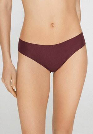 Mujer con ropa interior tipo bikini sin costuras de color púrpura oscuro, mostrando la sección media desde las caderas hasta debajo del pecho sobre un fondo liso.