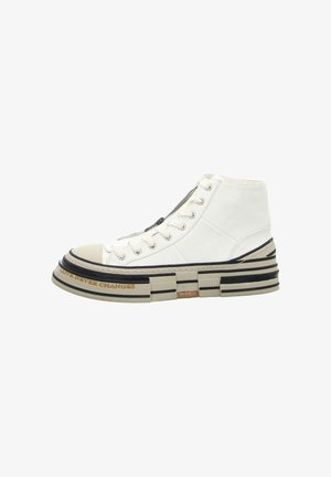 High-top sneaker in white leather with textured accents, thick multi-layered sole, black and beige stripes, and a prominent toe cap.