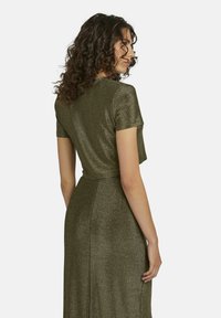 Metallisch grünes Kleid mit tailliertem Oberteil und kurzen Ärmeln. Der Stoff hat ein glänzendes, strukturiertes Finish und verjüngt sich zu einem fließenden Rock.