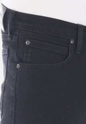 Vaqueros negros de denim con corte Slim que cuentan con cinco bolsillos, herrajes metálicos y un acabado texturizado. Etiqueta visible en la cinturilla.