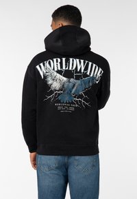 Schwarzer Hoodie mit einer großen Grafik eines Adlers und dem Wort "WORLDWIDE" in Weiß, versehen mit Blitzmotiven. Rippbündchen und -saum.