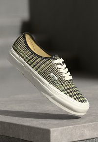 Canvas sneakers met een groen en beige houndstooth-patroon, witte veters en een witte rubberen zool. Het ontwerp heeft een zwarte rand rond de kraag.