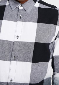 Schwarz-weiß kariertes Hemd mit Knopfleiste und regelmäßigem Kragen, aus strukturiertem Stoff gefertigt und mit kontrastierenden Knöpfen versehen.