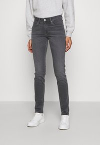 Vaqueros skinny de mezclilla gris con una cintura de tiro medio, sutiles marcas de desgaste y bolsillos frontales, combinados con zapatillas blancas y sudadera gris.