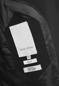 Etiqueta de ropa en el interior de una prenda negra que muestra la marca "Casual Friday", talla 50, ajuste slim y lema "Casual Friday se ha convertido en el nuevo casual de todos los días."