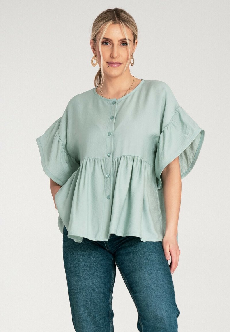 Jasnozielona bluzka z zapięciem na guziki z przodu, szerokimi rękawami i marszczoną talią. Wykonana z miękkiego materiału o luźnym kroju. Połączona z ciemnymi dżinsami.