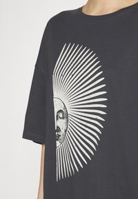 Tmavě modré oversized tričko z bavlny má velký bílý grafický motiv slunečního výbuchu se tváří ve středu. Krátké rukávy, kulatý výstřih.