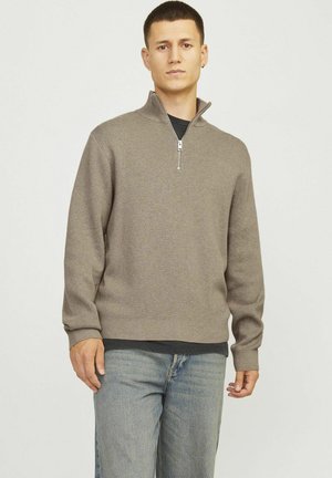 Bruine gebreide pullover met een kwart rits halslijn en geribbelde manchetten, gecombineerd met lichtblauwe denim jeans.
