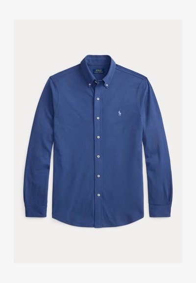 Kék hosszú ujjú, gombos pamuting, amely gallérral, gombos elülső résszel és a bal mellkas felett hímzett logóval rendelkezik.