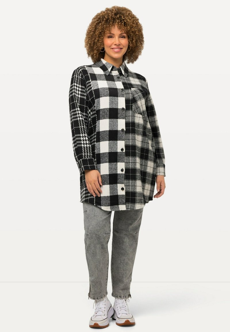 Svart och vit rutmönstrad skjortklänning med blandade mönster, långa ärmar, knäppning fram, kombinerad med grå jeans och vita sneakers.