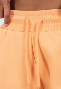 Orange sweatsbukser med ribbet talje, elastisk snor og sidelomme. Blød tekstur, afslappet design med minimal detaljer.