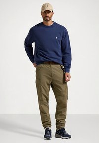 Marineblå genser, olivengrønne cargobukser, beige caps og marineblå joggesko. Merkbare detaljer: logo på genser, cargolommer på bukser.