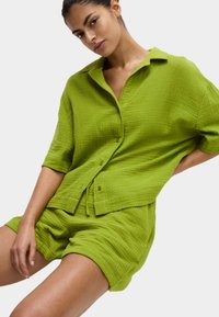 Camicetta verde a maniche corte con texture, abbinata a pantaloni corti coordinati, entrambi caratterizzati da una vestibilità rilassata e una texture del tessuto stropicciata.