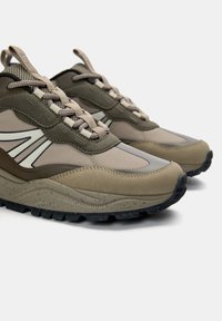 Beige und olivgrüne Sneakers aus Netz- und Synthetikmaterialien, mit runder Zehenform, strukturierten Schnürsenkeln und einer stabilen Gummisohle mit Profil.