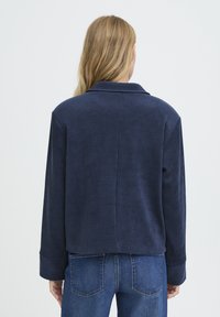 Veste en velours côtelé marine avec col et manches longues, présentant des rayures verticales, une coupe décontractée et une taille raccourcie.