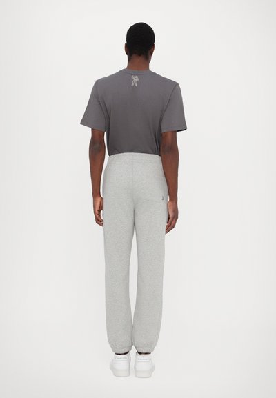 Grey cotton blend sweatpants with elastic cuffs, featuring a side pocket and logo detail. Paired with a short-sleeve grey t-shirt.